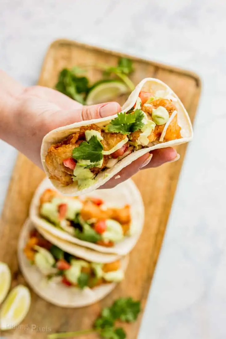 Fresh fish tacos with cilantro, lime, and avocado on a wooden serving board.